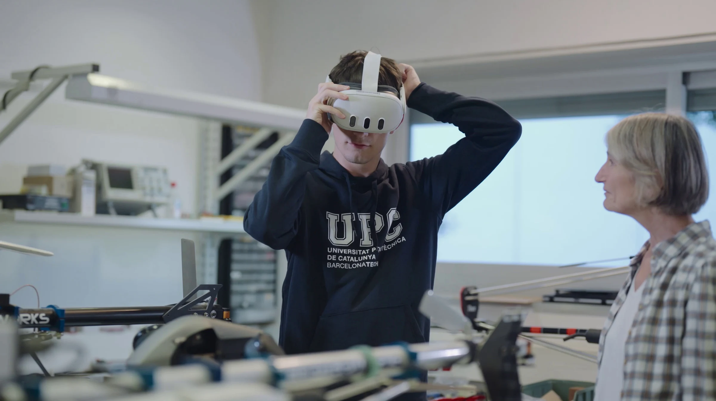 En un laboratorio, un estudiante de la UPC se ajusta un visor de realidad virtual mientras una profesora lo observa.