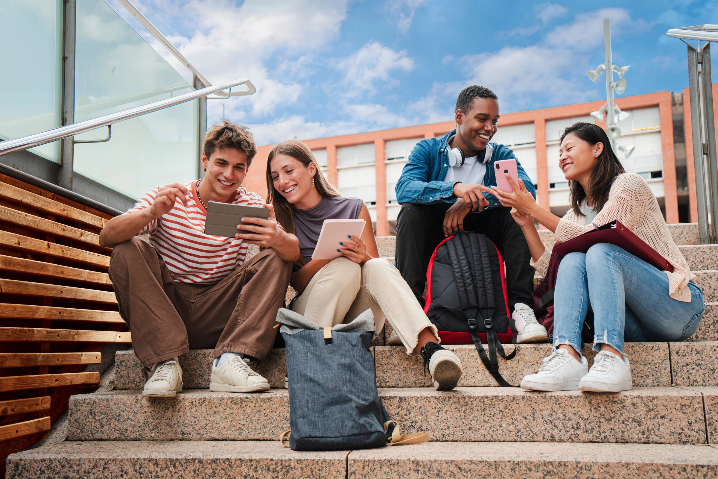 Four young people talk about the contents of a mobile phone and a tablet sitting on the steps of the UPC's Barcelona-North Diagonal Campus.
